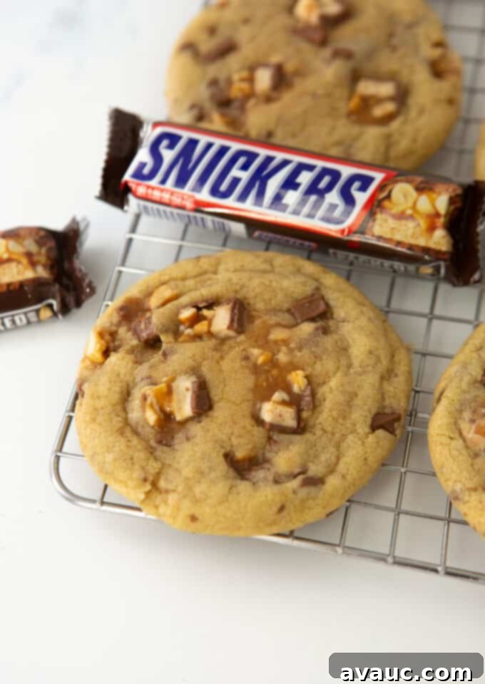 Decadent Chewy Snickers Cookies 2 Soft and chewy Snickers cookies cooling on a wire rack with whole Snickers bars nearby