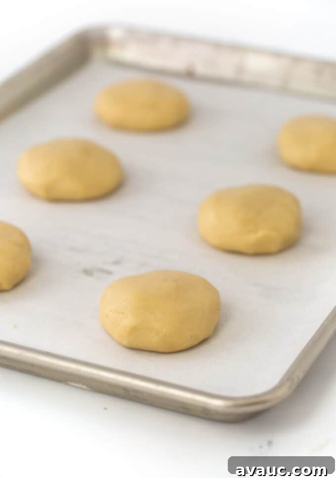 Coconut Cloud Sugar Cookies 6 Unbaked coconut sugar cookie dough balls, flattened into discs, arranged on a parchment-lined cookie sheet.