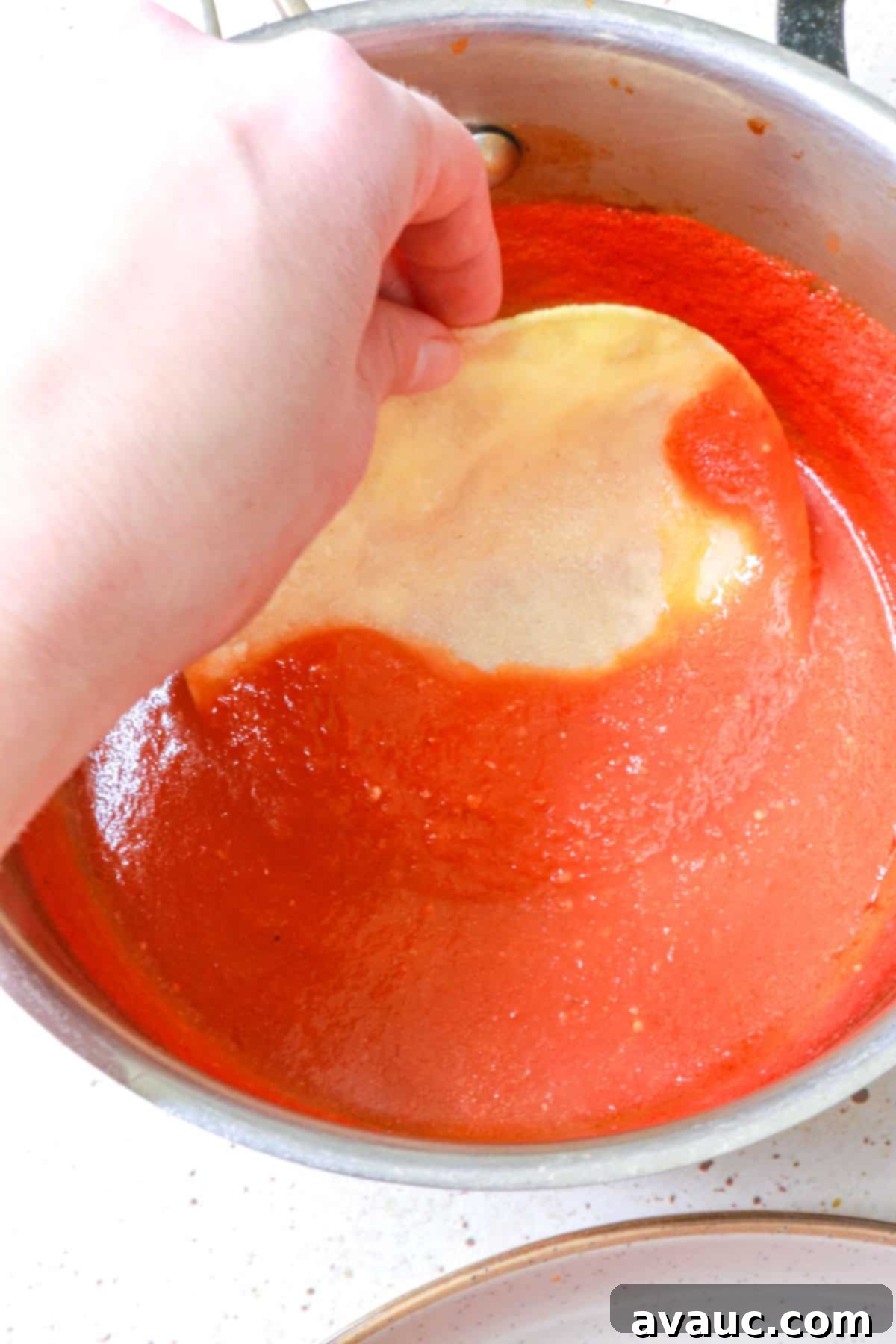 a hand dipping a corn tortilla in tomato sauce