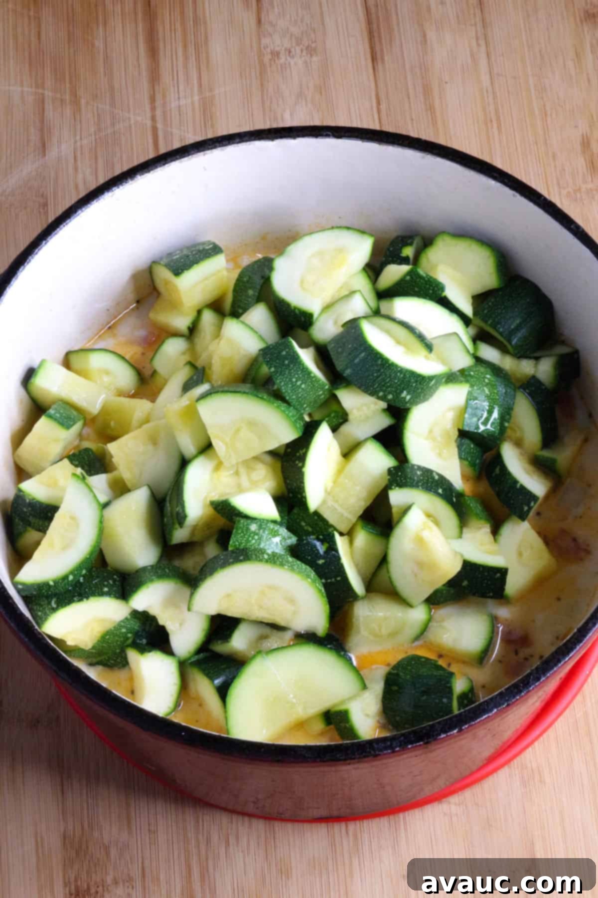 Cheesy Calabacitas 8 Re-introducing parboiled zucchini into the creamy corn and vegetable mixture in a red pot