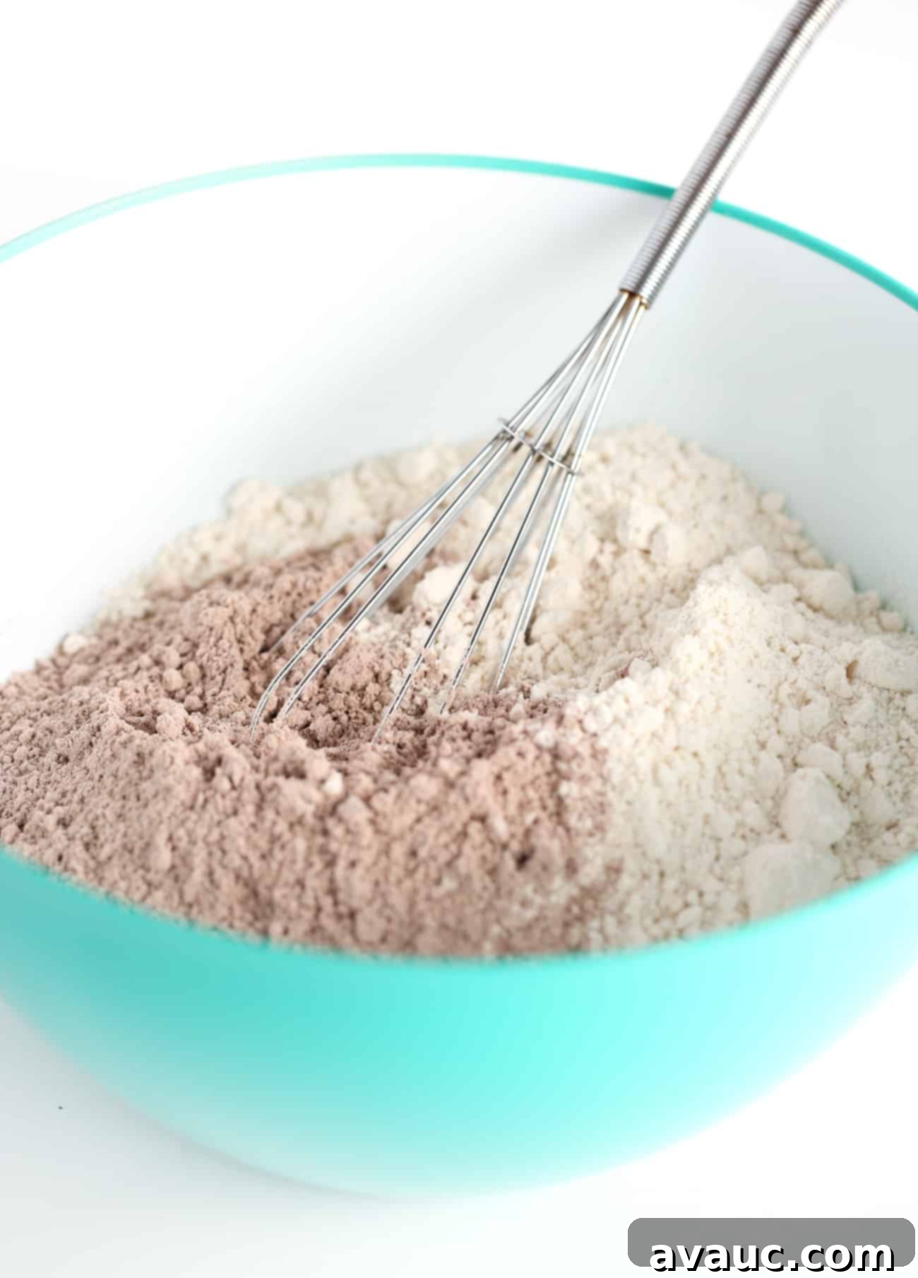 Metal whisk stirring blue bowl of brownie mix and Bisquick pancake mix for chocolate brownie cookies, highlighting the initial dry ingredient combination.