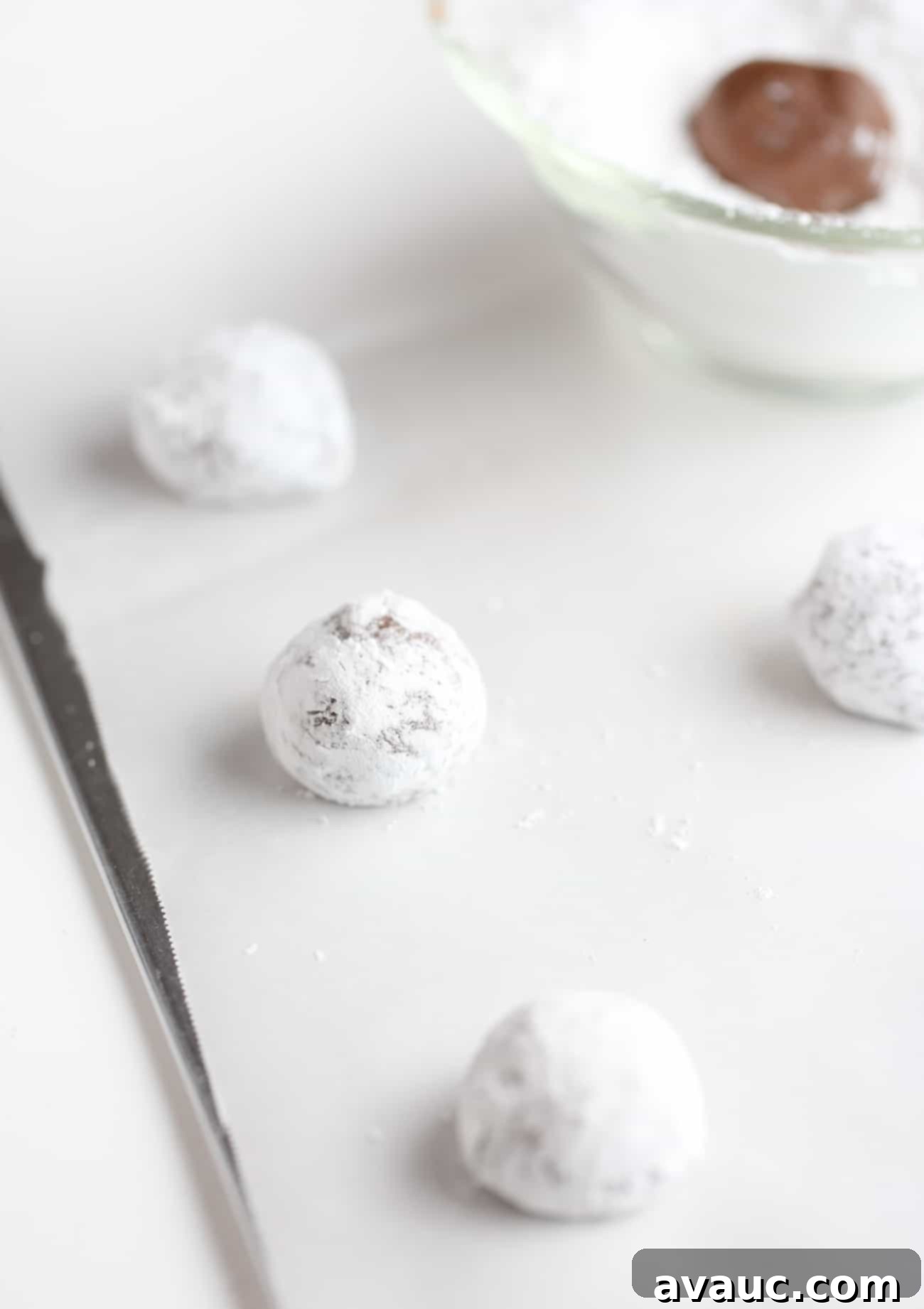 Balls of chocolate brownie cookie dough, perfectly coated in powdered sugar, arranged on a cookie sheet, ready for baking.