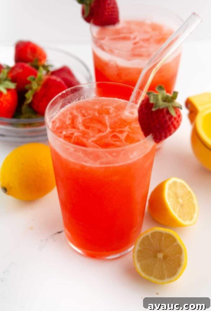 Easy Strawberry Lemonade 2 Glass of vibrant homemade strawberry lemonade with fresh strawberry and lemon slices as garnish, sitting on a wooden table.