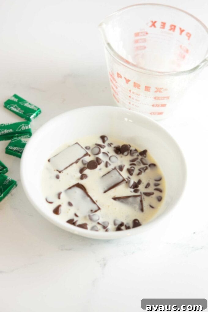 white bowl of chocolate chips and andes mint candies covered with hot heavy cream
