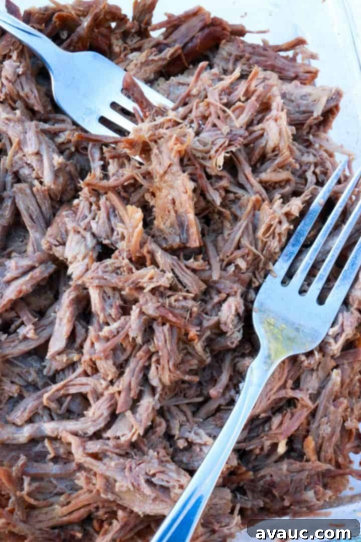 Close-up of a fork gently pulling apart tender strands of shredded beef, demonstrating its perfect cooked texture and juicy consistency, ready for various dishes.