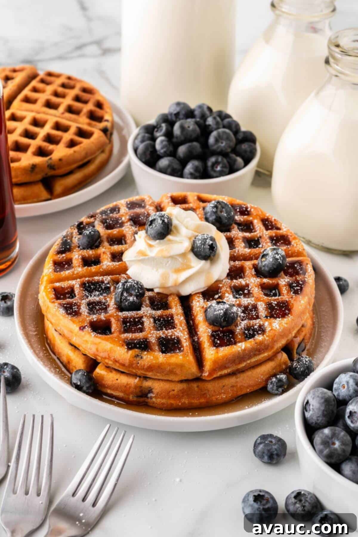 Golden Blueberry Crunch Waffles 2 Blueberry waffles with whipped cream and blueberries on top, served on a white plate.