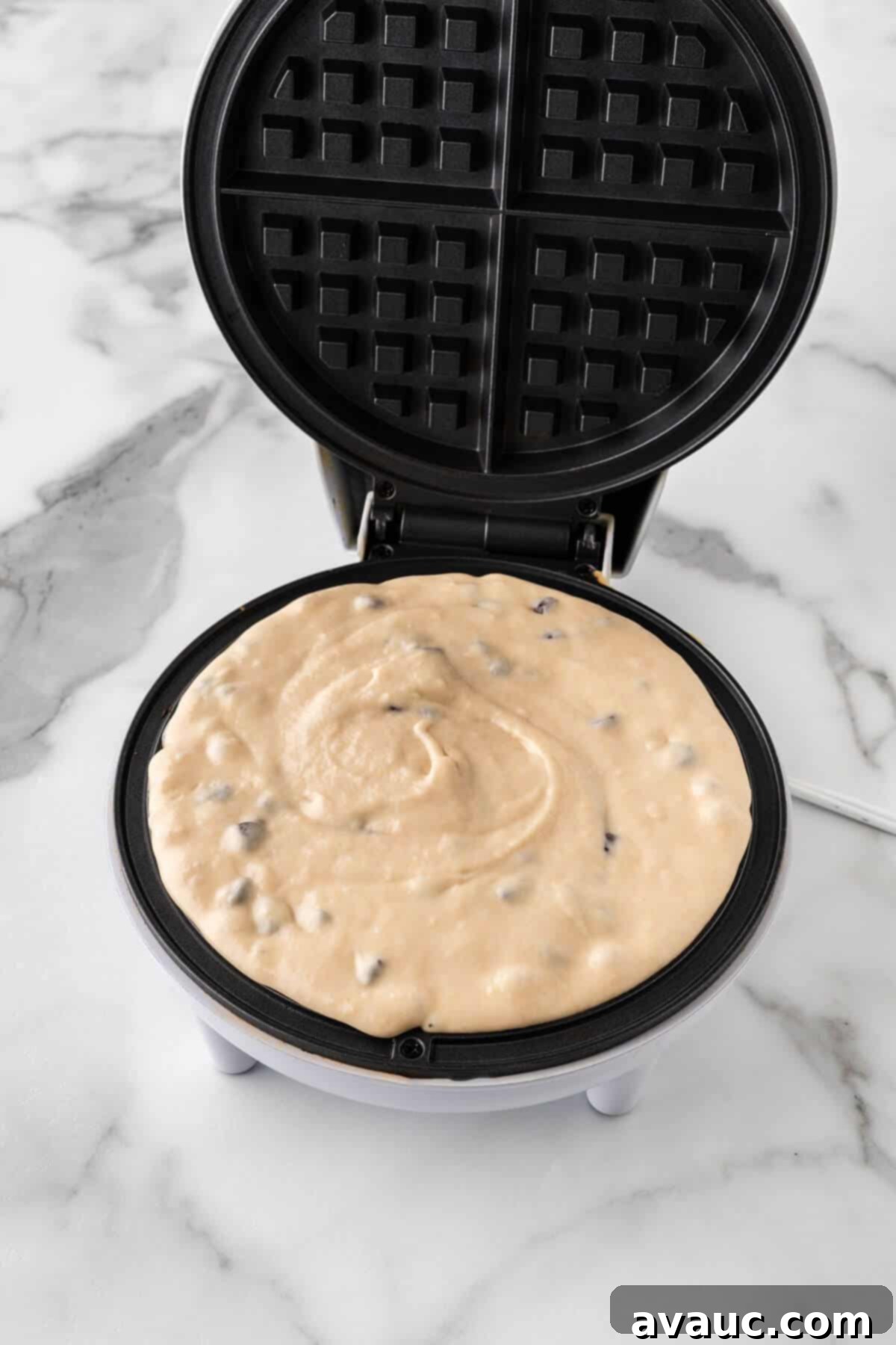 Golden Blueberry Crunch Waffles 14 Blueberry waffle batter evenly spread in a hot waffle iron, ready to cook.