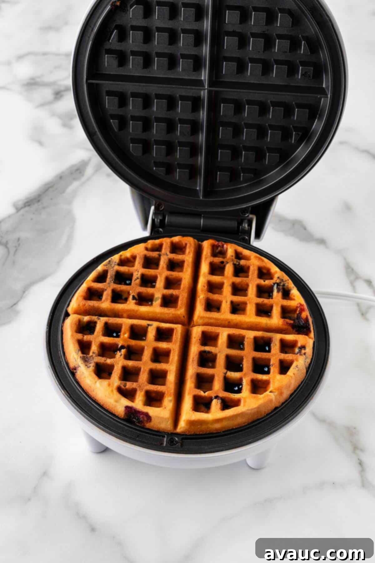 Golden Blueberry Crunch Waffles 15 A golden-brown blueberry waffle cooking in a waffle iron, almost ready.