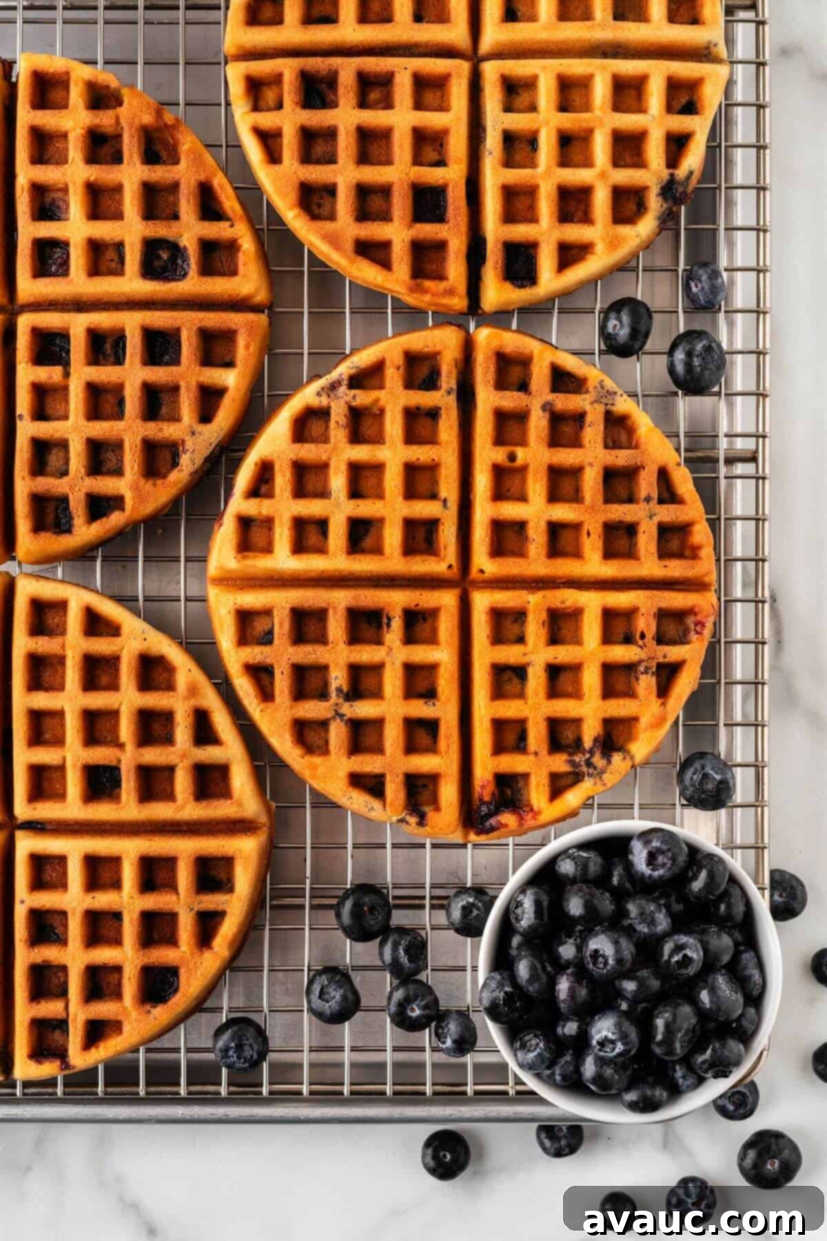 Golden Blueberry Crunch Waffles 16 A stack of crispy blueberry waffles on a wire cooling rack, with a cup of fresh blueberries on the side.