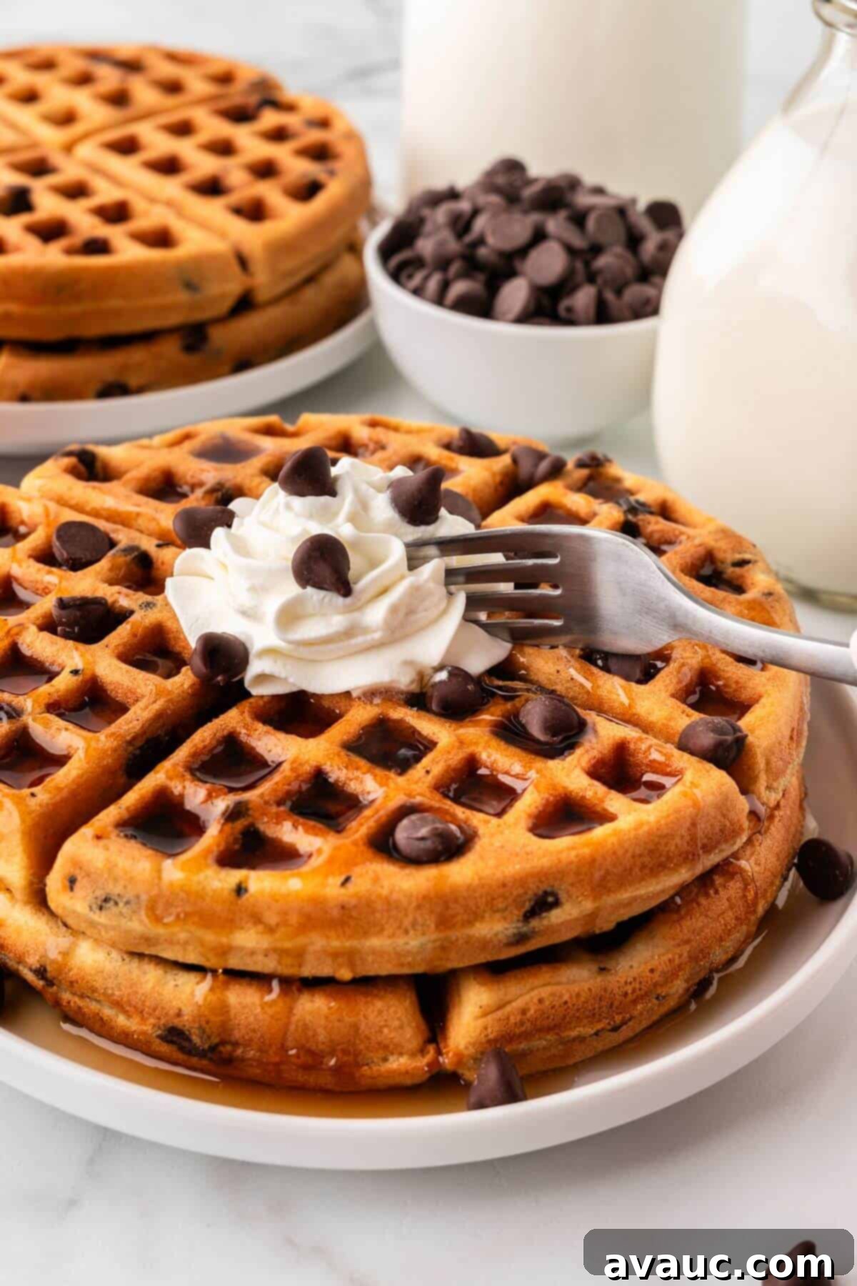 Sweet Morning Chocolate Chip Waffles 2 Fork cutting into stack of chocolate chip waffles with whipped cream, showing their fluffy interior and melty chocolate chips.