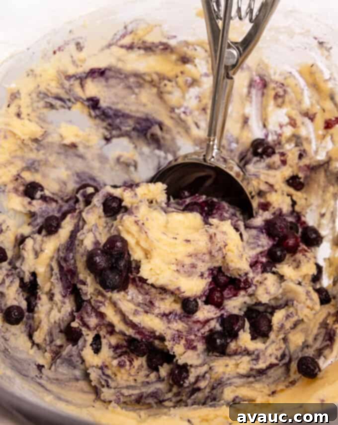 Bowl of mixed blueberry muffin batter with a cookie scoop, demonstrating the scooping process.