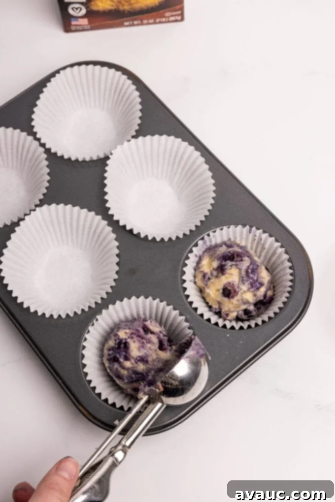 Scooping blueberry muffin batter into a jumbo muffin pan lined with paper cups.