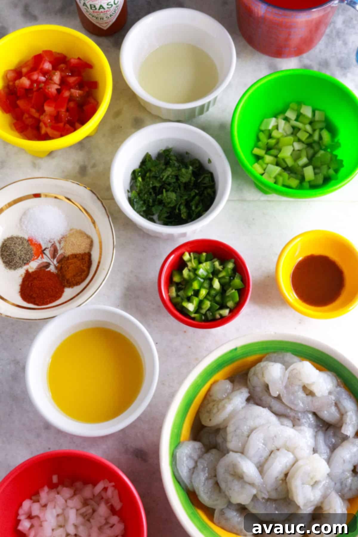 Vibrant Mexican Shrimp Cocktail 3 Tabasco sauce bottle, measuring cup with tomato juice, bowls with diced tomato, cilantro, lime juice, celery, spices, diced jalapeño, hot sauce, orange juice, raw shrimp and diced onion.