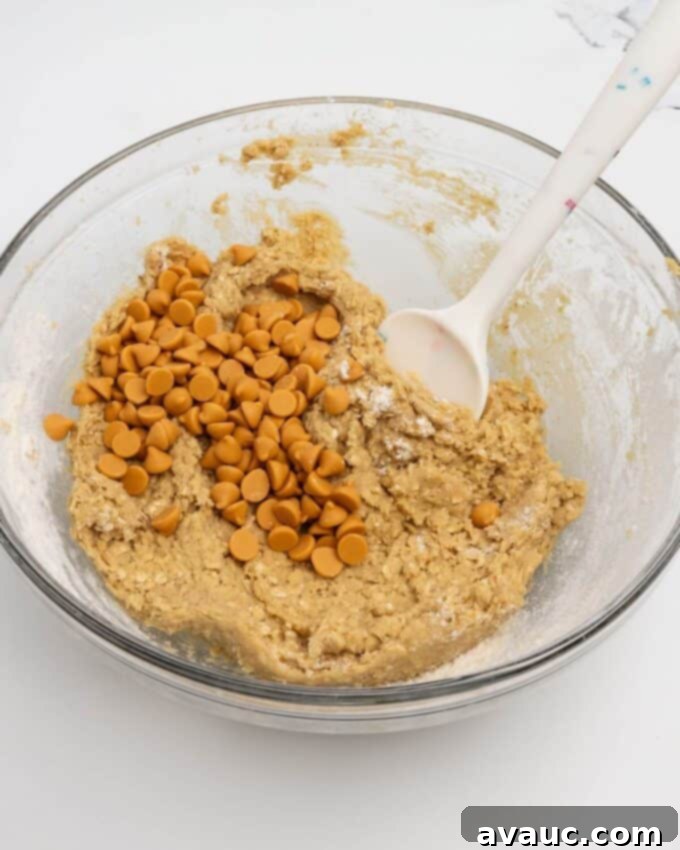 Homemade Chewy Oatmeal Scotchies 4 adding butterscotch chips to oatmeal scotchie dough in glass mixing bowl with rubber spatula