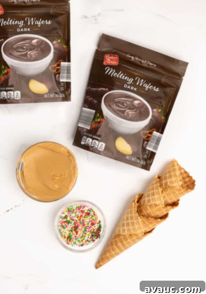 Christmas Nutty Buddy Bark 3 A flat lay photograph showcasing the four simple ingredients for Nutty Buddy bark: dark chocolate melting wafers, creamy peanut butter, waffle cones, and colorful sprinkles.