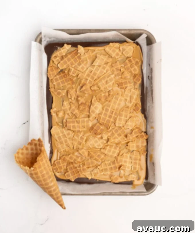 Christmas Nutty Buddy Bark 7 Broken waffle cone pieces pressed into the soft peanut butter layer of the chocolate bark, creating a crunchy texture.