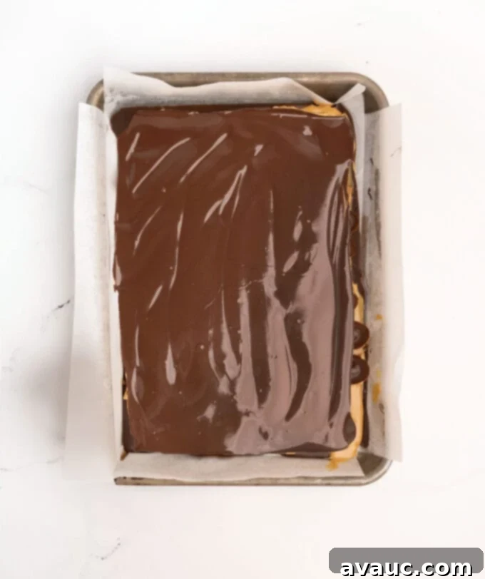 Christmas Nutty Buddy Bark 9 A spatula carefully spreading the final layer of melted dark chocolate over the waffle cones, creating a smooth top surface for the bark.