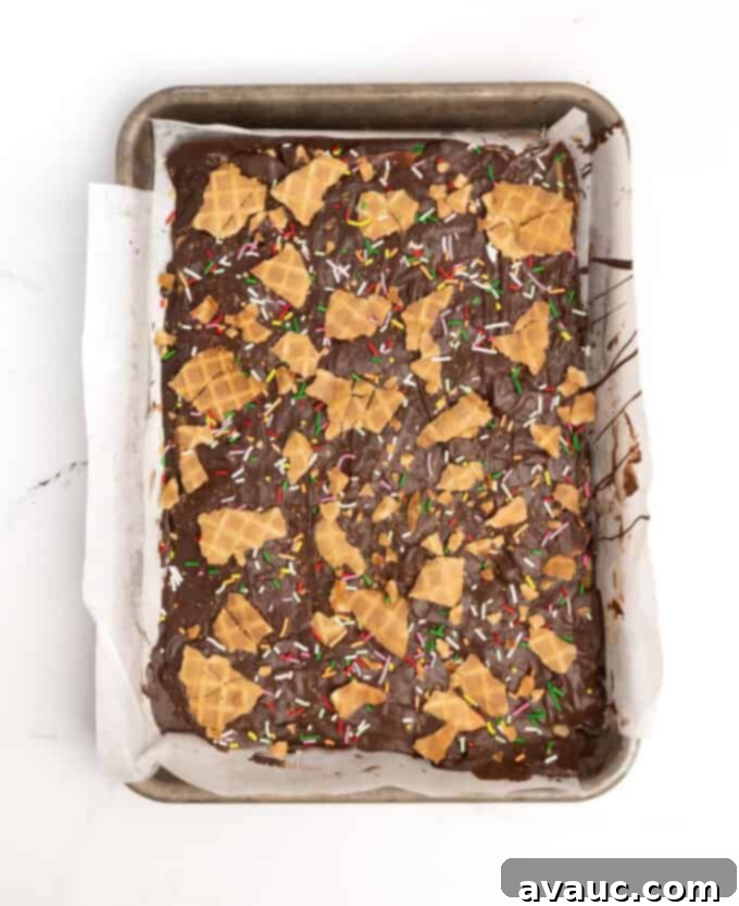 Christmas Nutty Buddy Bark 10 A sheet of finished chocolate peanut butter bark adorned with colorful Christmas sprinkles and additional waffle cone pieces, freshly set and ready to be broken.