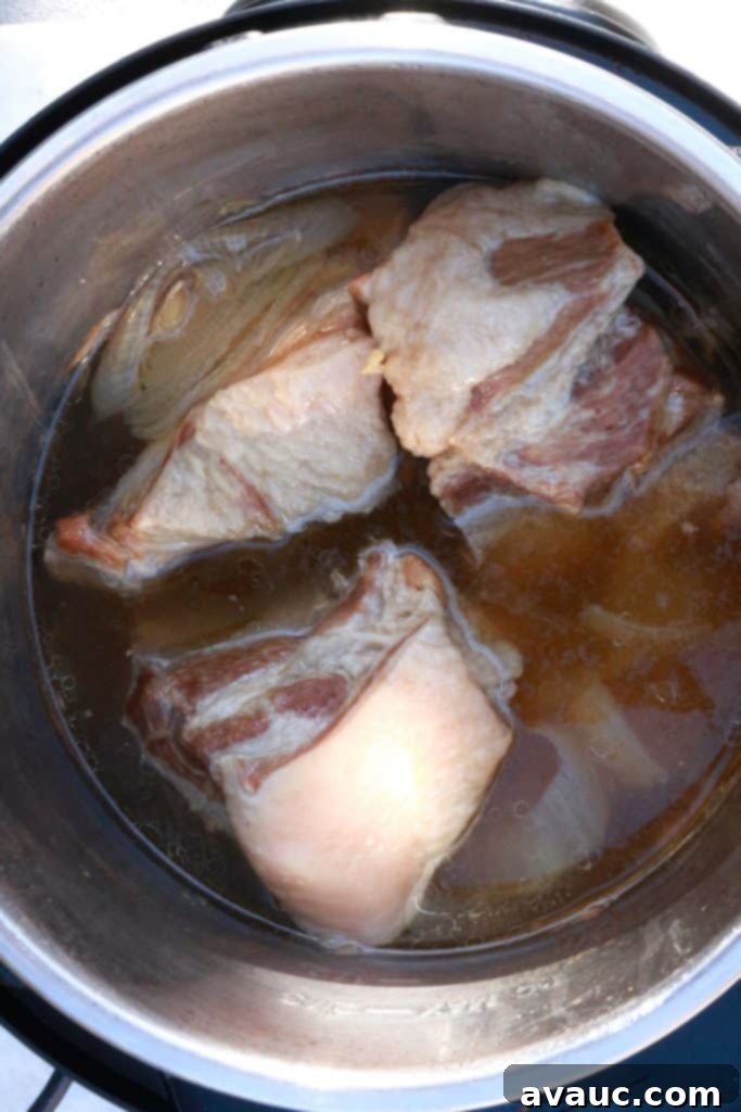 Crispy Golden Carnitas 4 Large pieces of pork shoulder with onion, garlic, and broth in a slow cooker, ready for cooking.