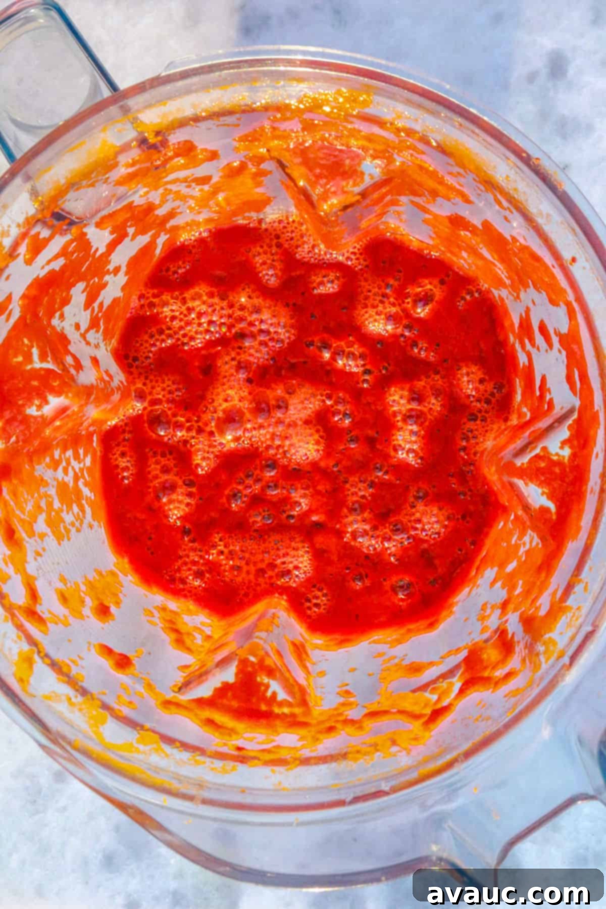 Top view of a blender filled with a vibrant red chile sauce, ready to be strained