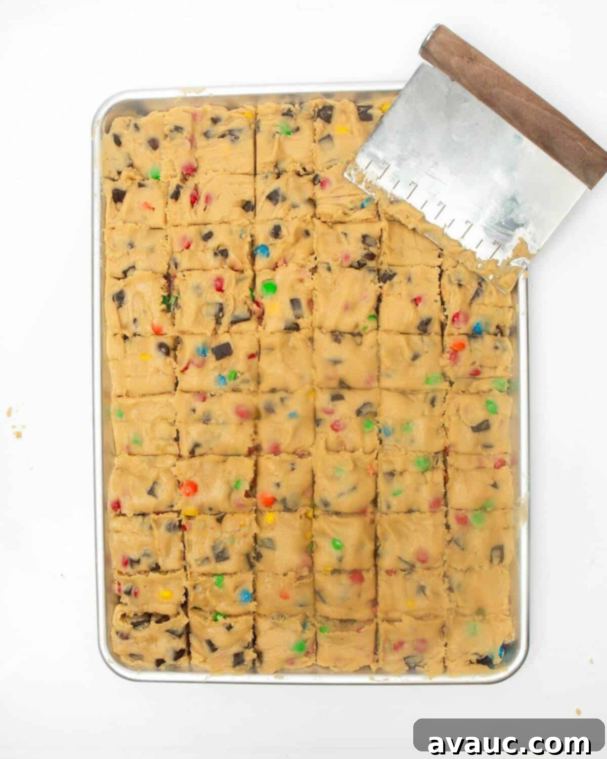 Using a bench scraper to precisely cut the spread-out cookie dough into uniform squares directly in the metal pan.