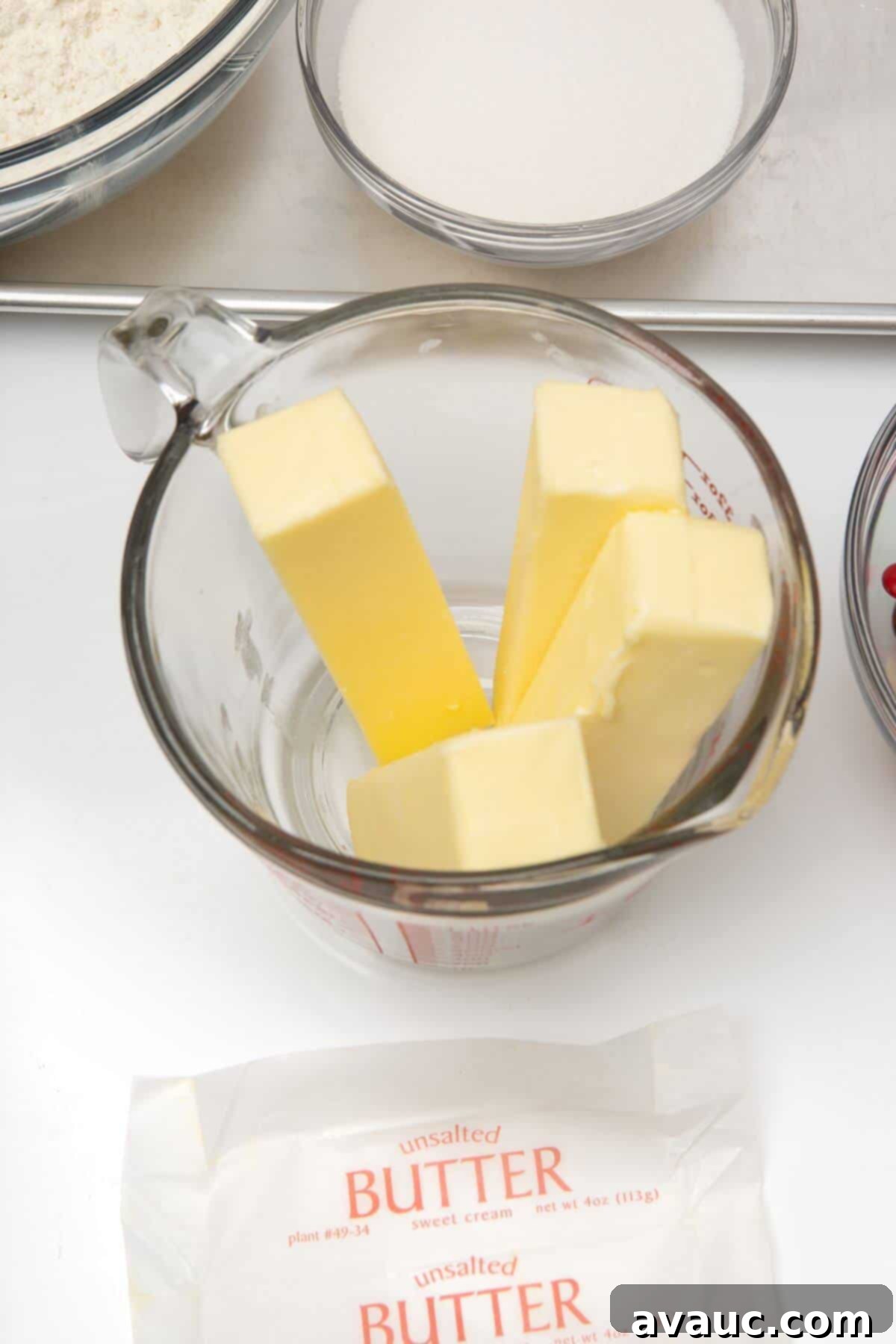 Four sticks of unsalted butter in a clear glass measuring bowl, ready for melting.