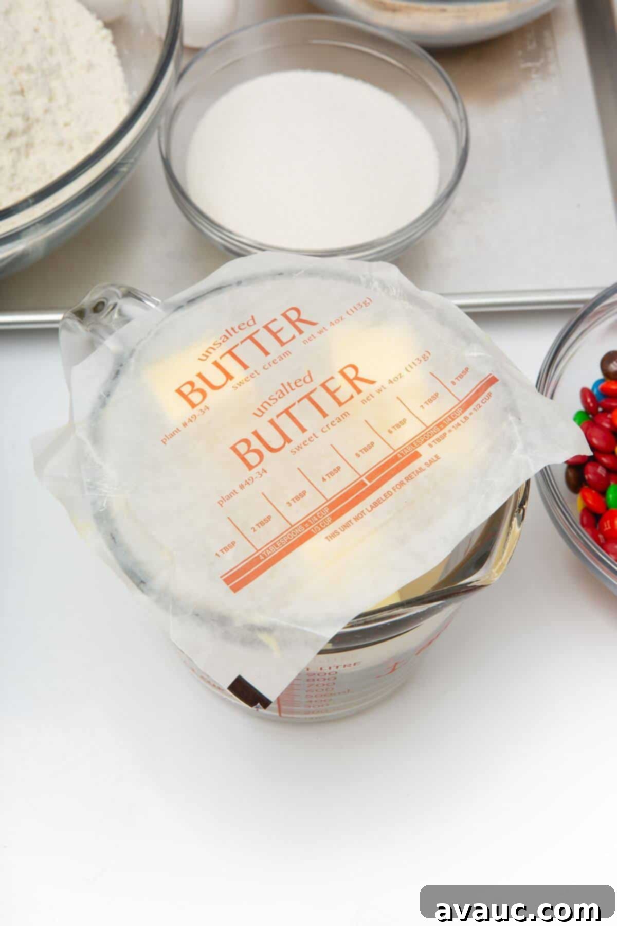 Melted butter in a glass measuring bowl, partially covered with butter wrappers to prevent microwave splatter.