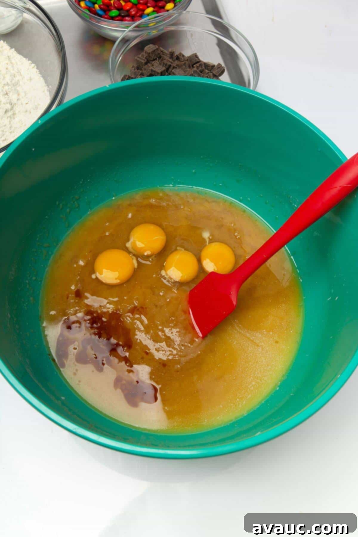 Wet ingredients for freezer cookie dough, including eggs and vanilla extract, thoroughly mixed in a green mixing bowl with a spatula.