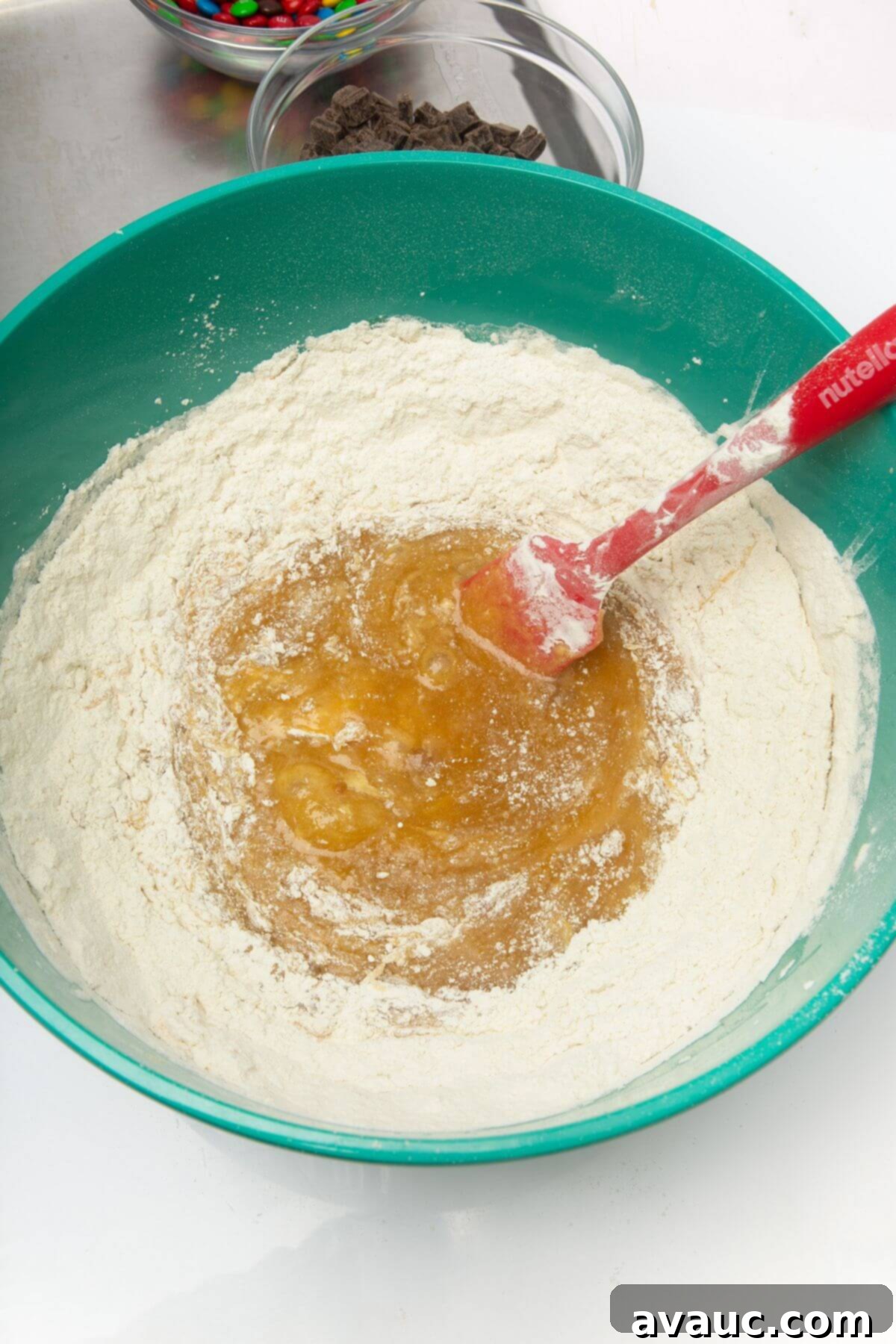 All-purpose flour being added to the wet ingredients in a mixing bowl with a spatula for freezer cookie dough.