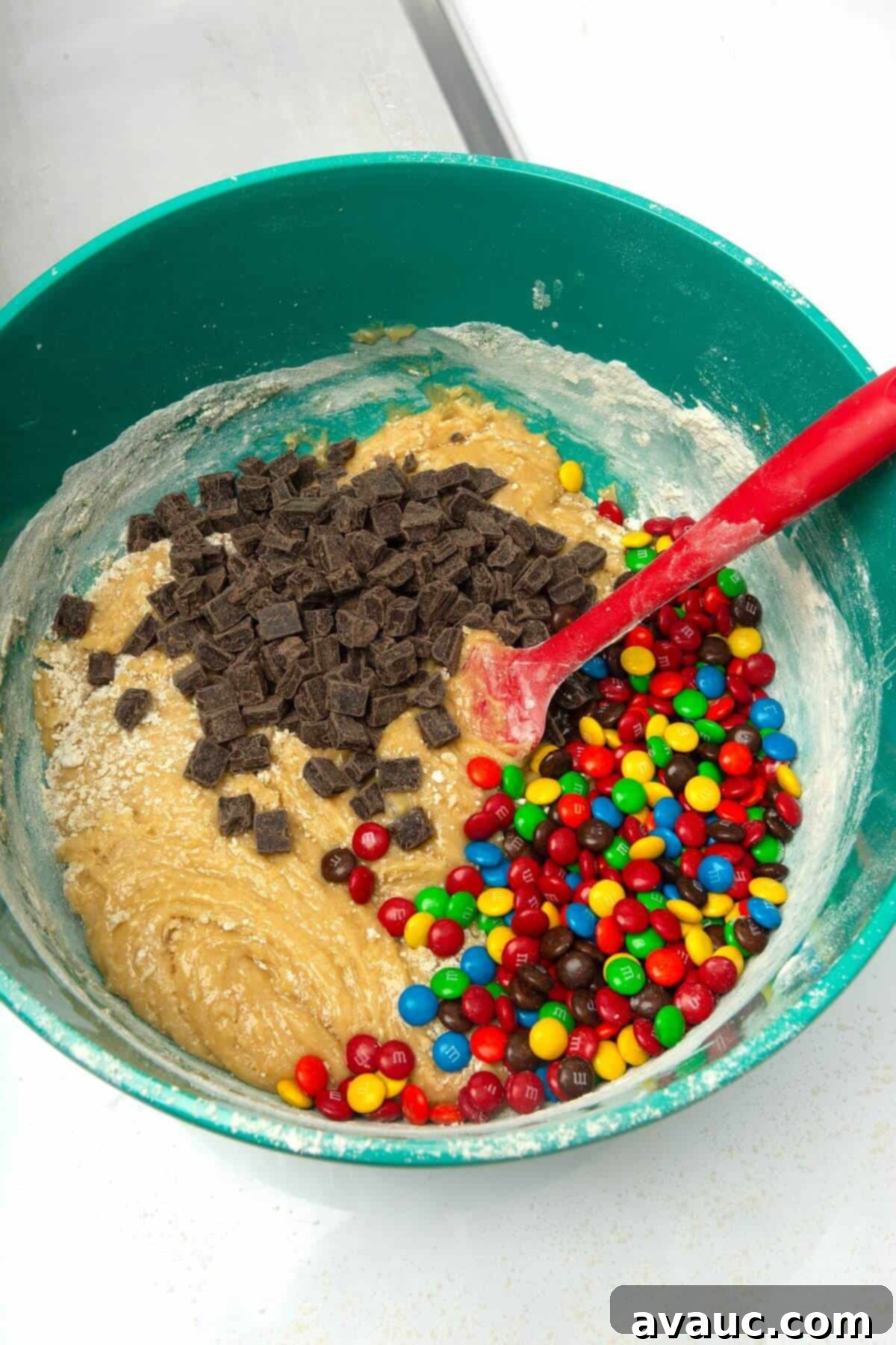 Chocolate chips and other mix-ins folded into the cookie dough in a mixing bowl with a spatula.