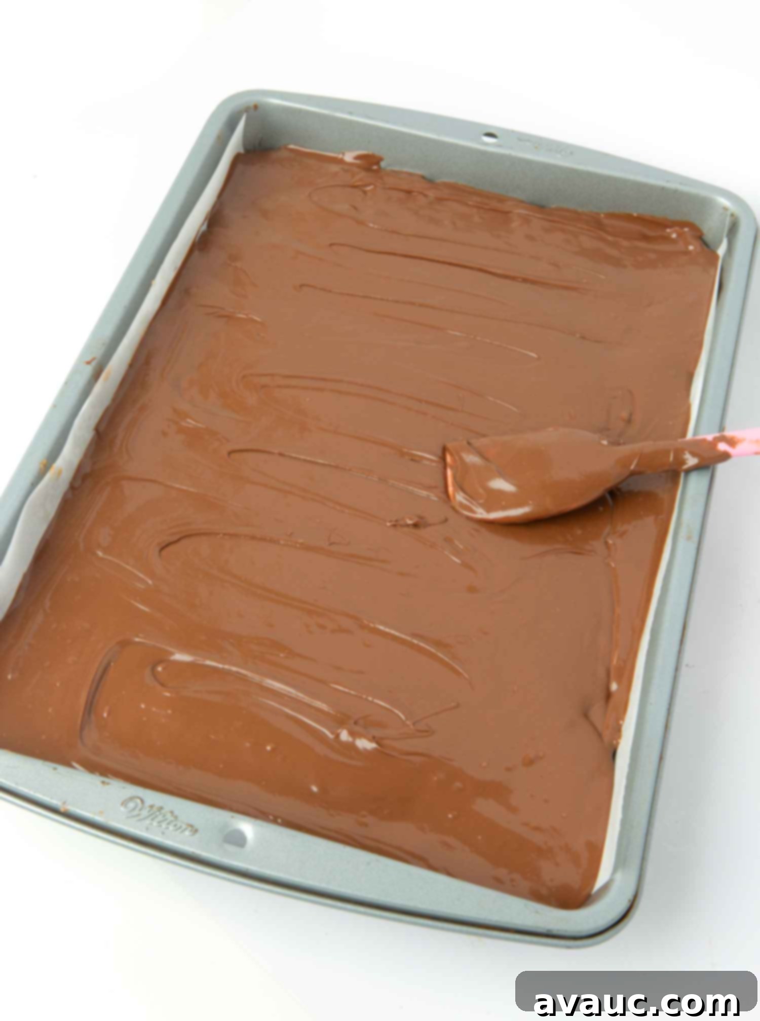 spreading the melted chocolate and butterscotch topping evenly over scotcheroo bars in a pan