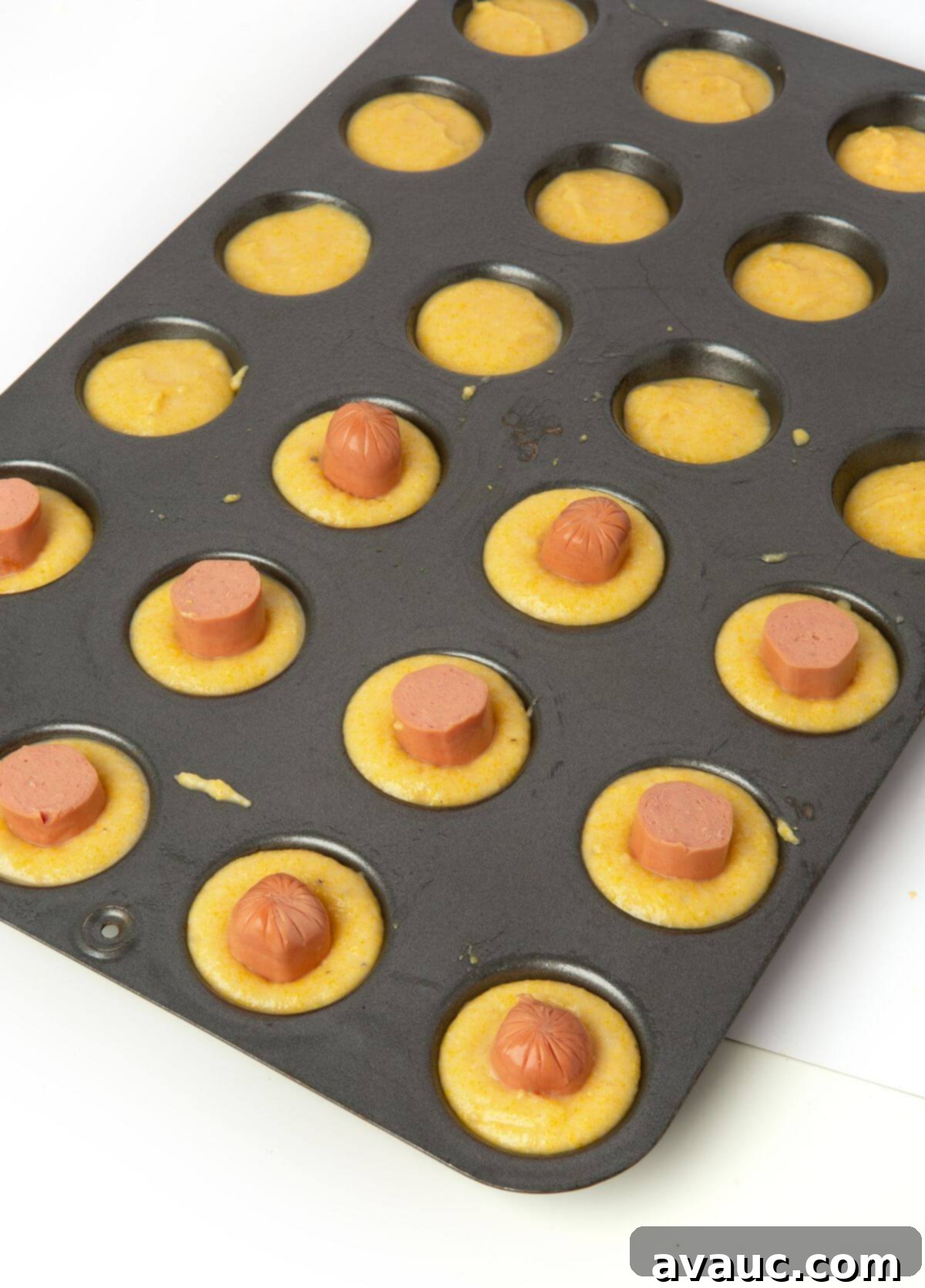 Corn Dog Muffin Poppers 7 Hot dog pieces gently pressed into corn muffin batter in a mini muffin tray, ready for baking