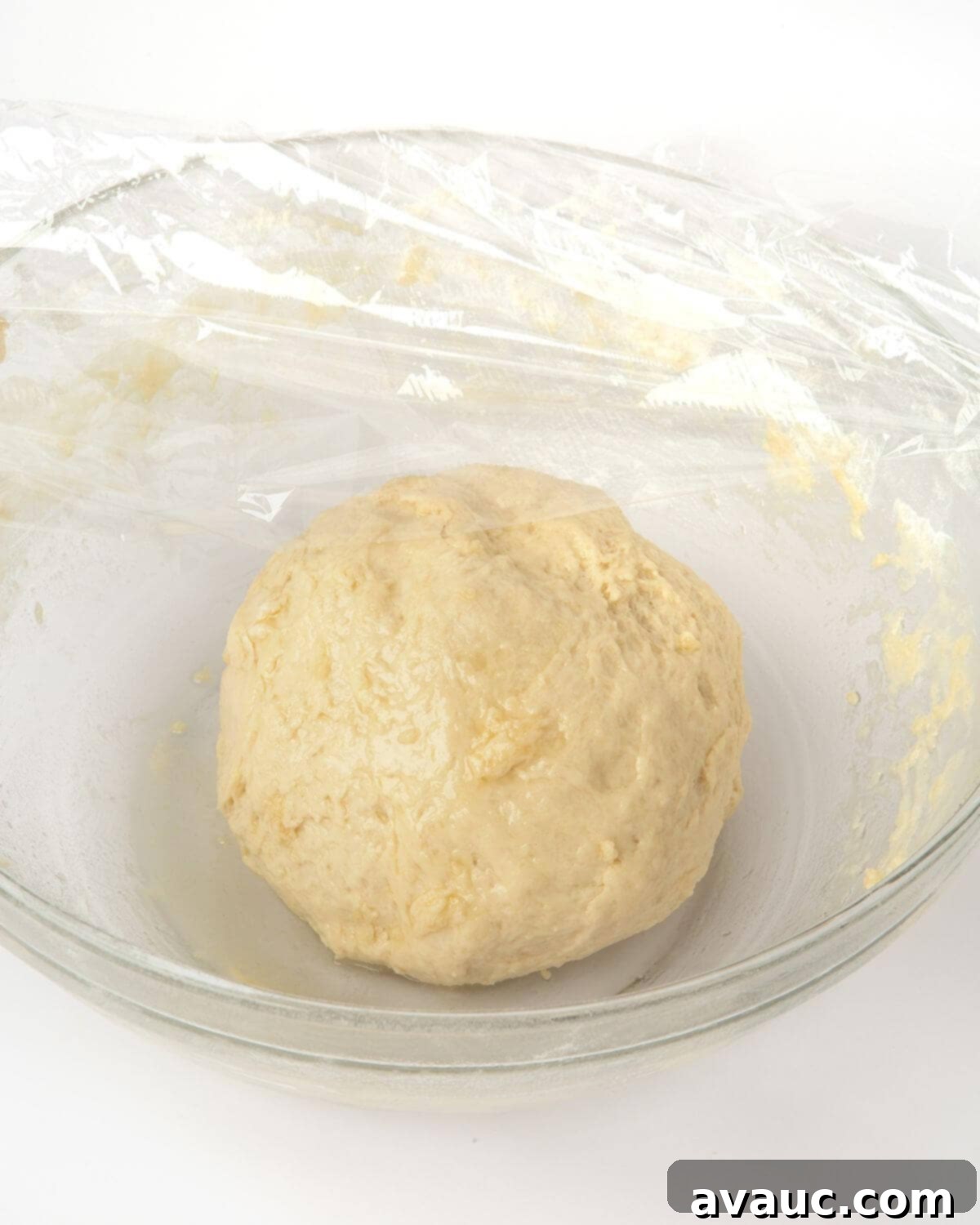 Smooth pretzel dough ball in a bowl, covered with plastic wrap for resting.