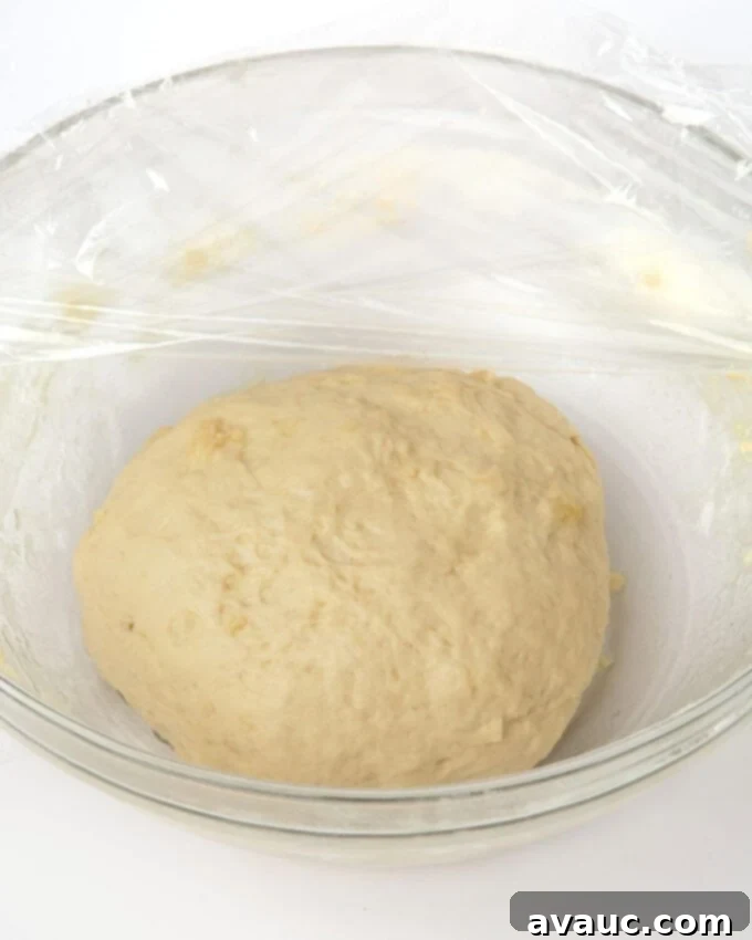 Proofed pretzel bite dough in a glass bowl, covered with plastic wrap.