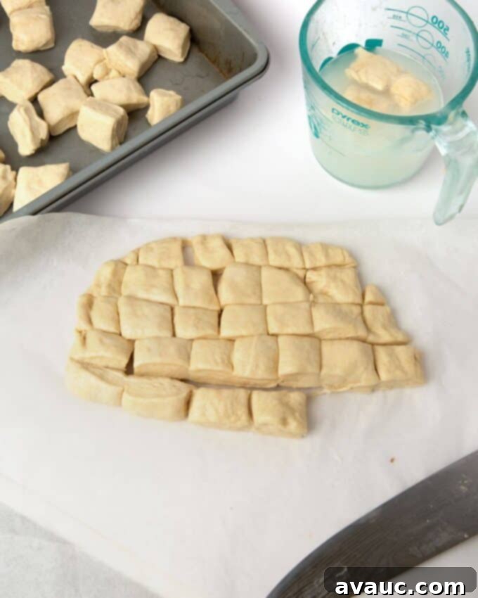 Pretzel monkey bread dough squares being dipped into a baking soda bath.