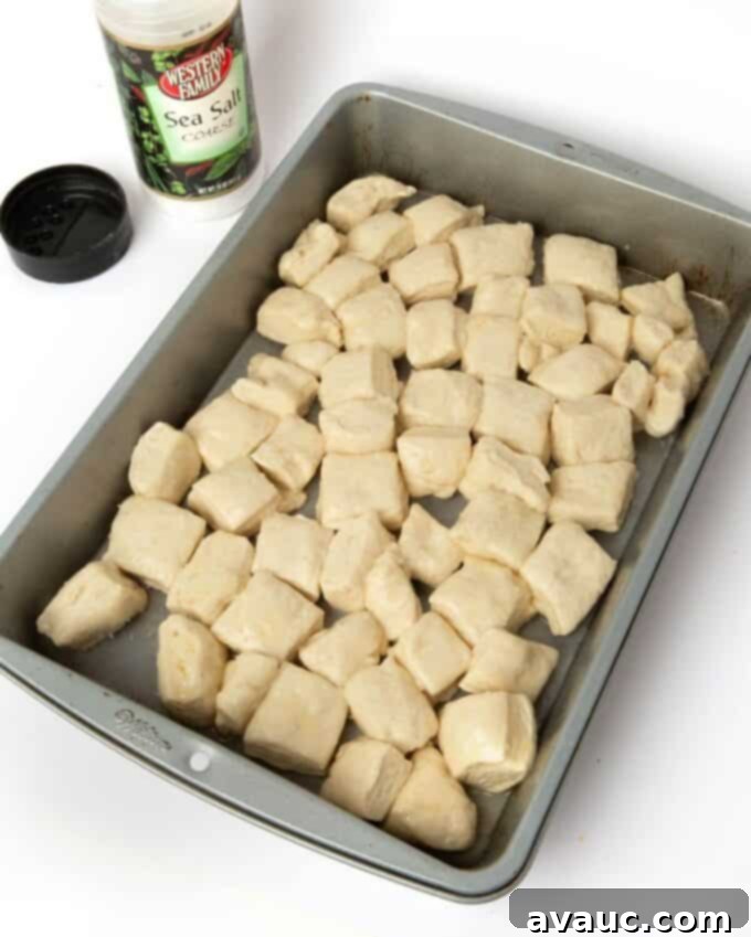 Pretzel monkey bread dough cubes arranged in a 9x13 baking pan, sprinkled with salt.