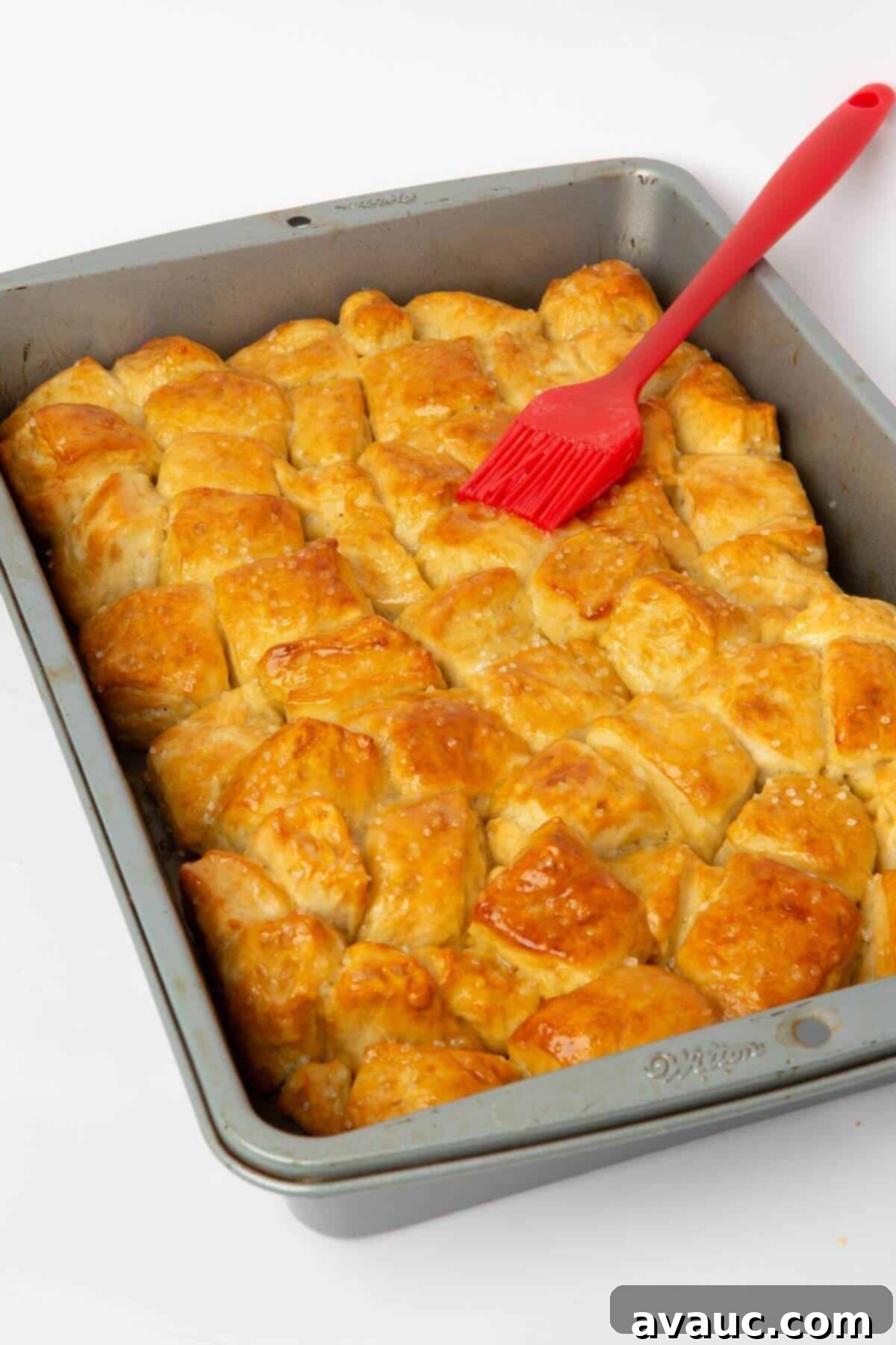 Freshly baked pretzel bite monkey bread in a pan, being brushed with melted butter.
