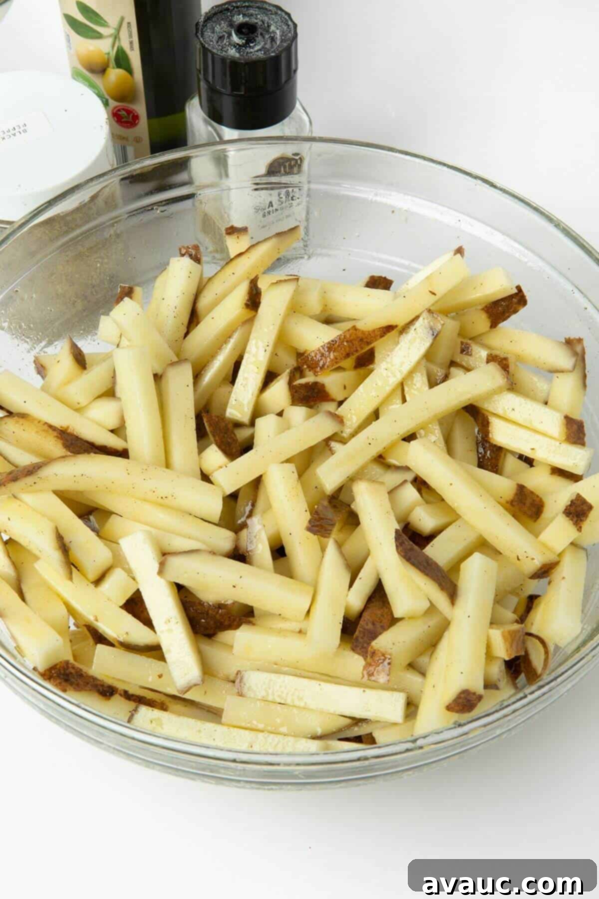 Potato fries tossed with olive oil and seasonings in a glass mixing bowl