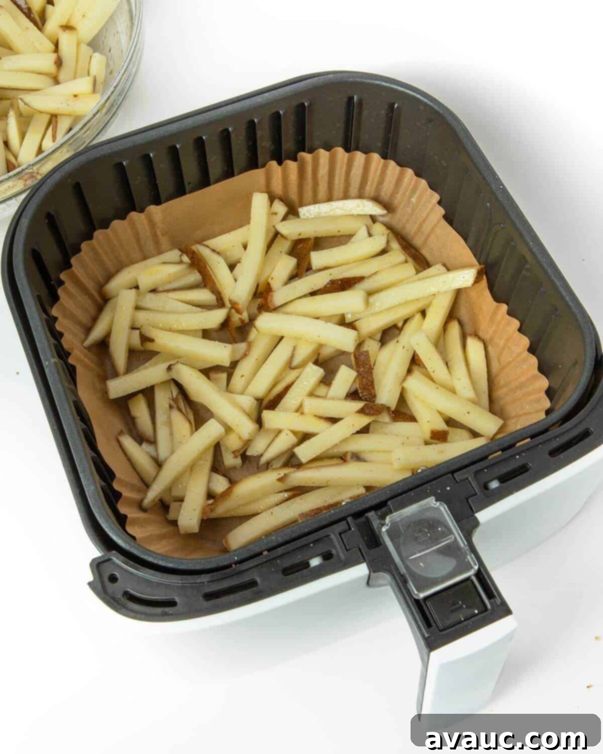 Seasoned potato fries arranged in a single layer in an air fryer basket with a paper liner