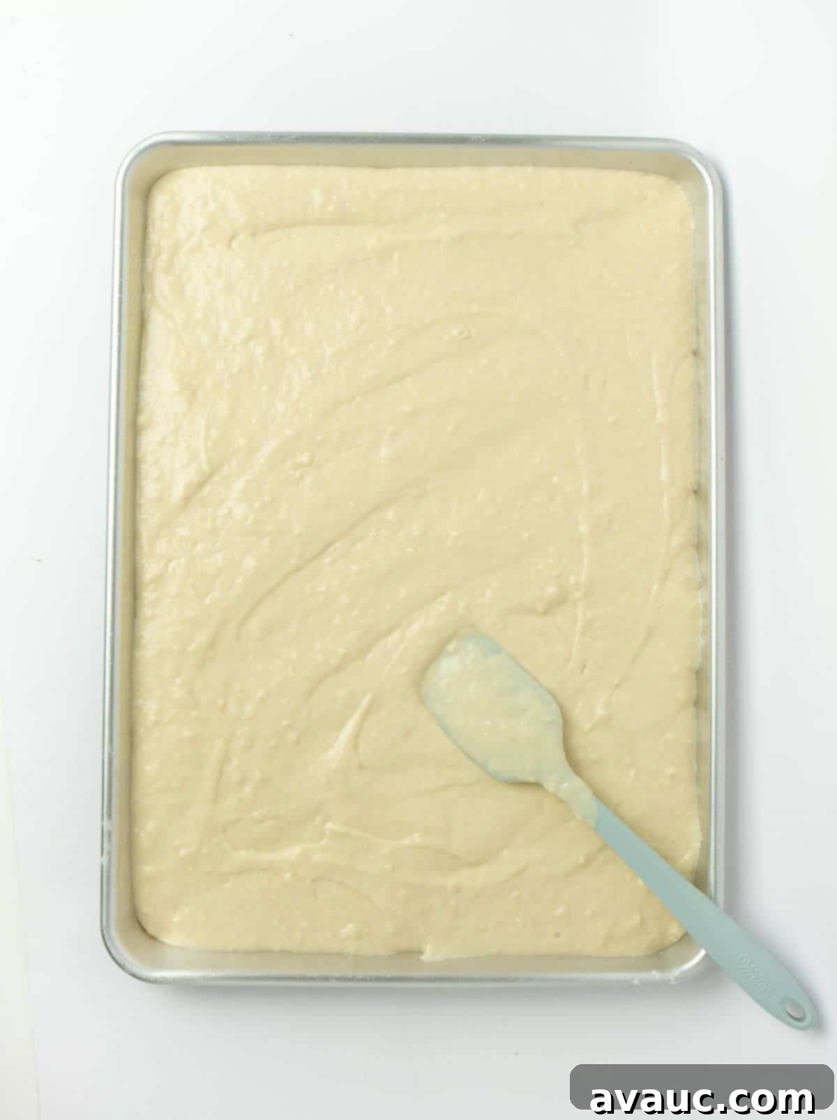 Sheet Pan Pancake Perfection 7 Pancake batter spread evenly on a parchment-lined sheet pan with a rubber spatula, ready for baking.