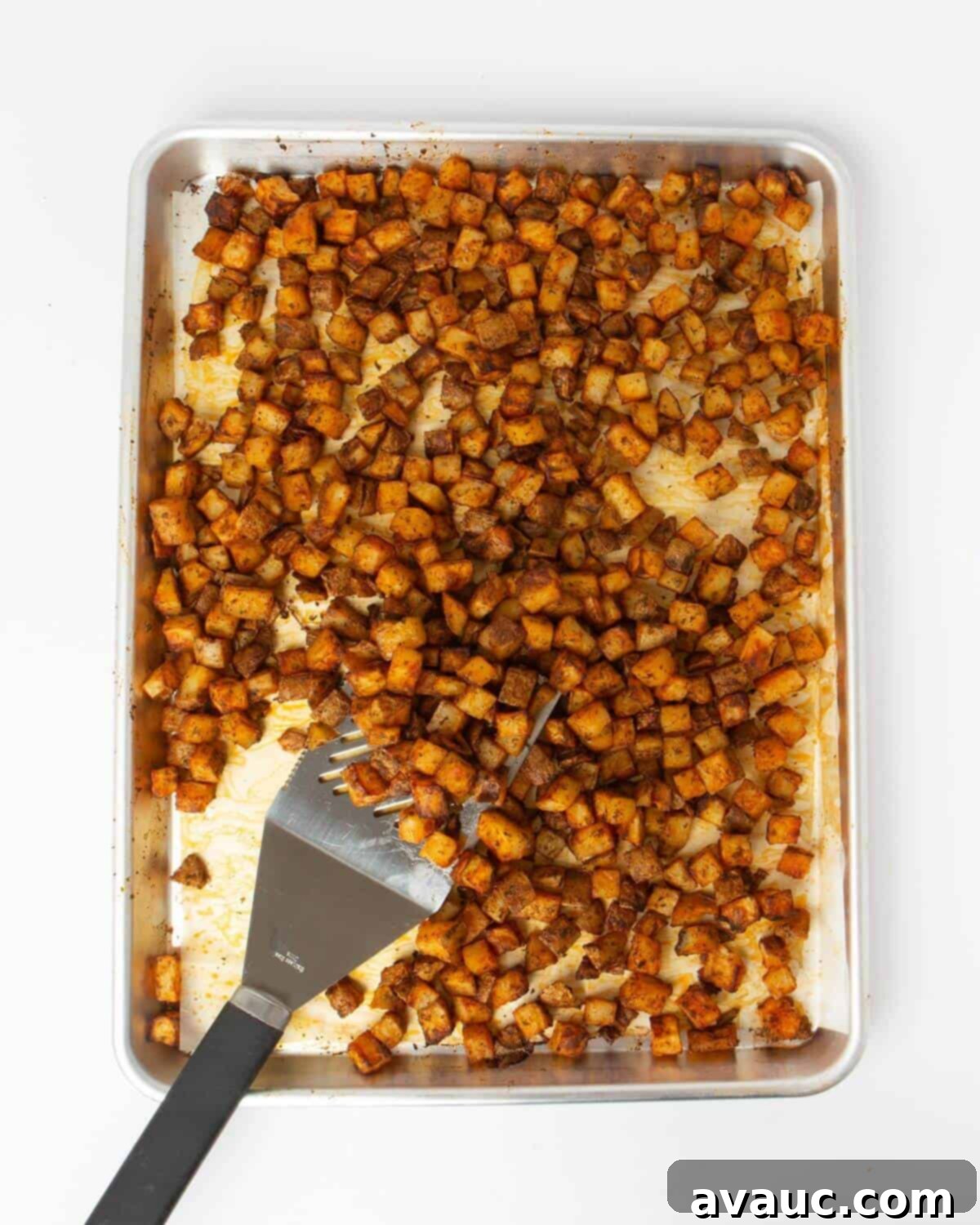 cooked breakfast potatoes on sheet pan lined with parchment paper and metal spatula