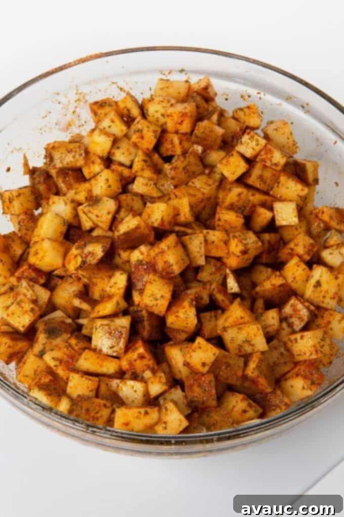 potatoes mixed with oil and seasoning in glass mixing bowl