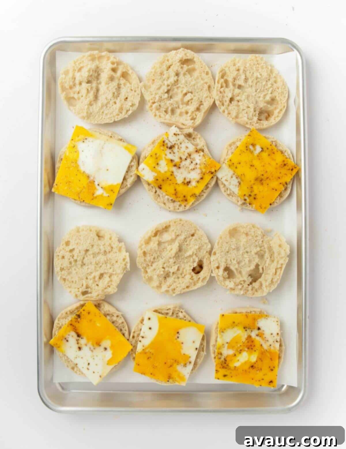 opened english muffins on baking sheet with sheet pan eggs on top of half