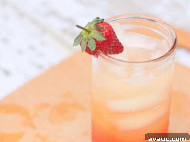 Close-up of a vibrant Orange Berry Spritzer with beautiful layers, garnished with strawberries. Design Eat Repeat