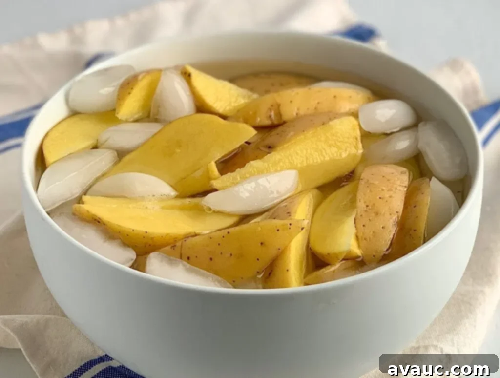 Golden Crispy Potato Wedges 4 Potato wedges in a large bowl filled with ice water.