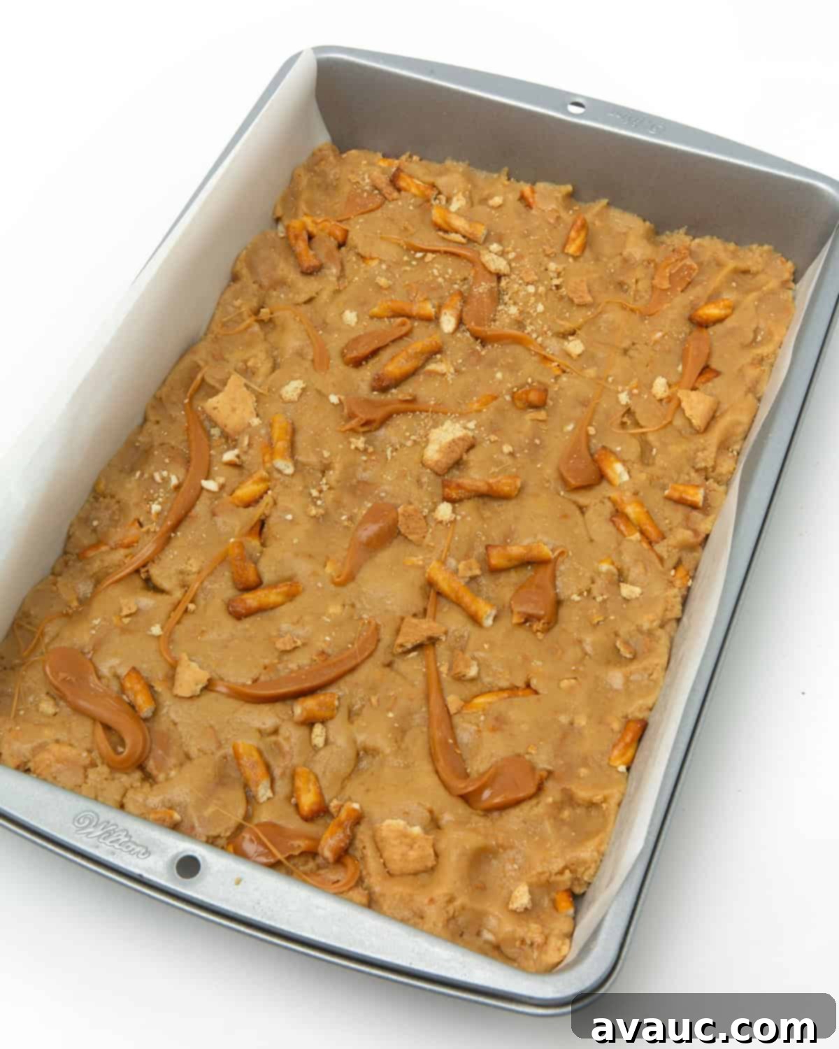 pan of unbaked caramel apple kitchen sink cookie bars topped with extra mix-ins