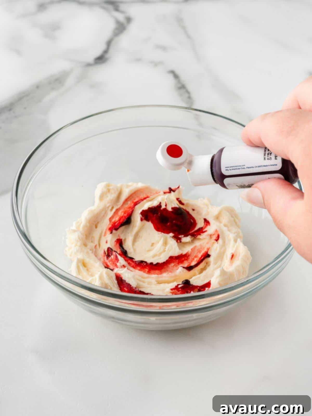 Adding red gel food dye to white buttercream frosting in a small glass bowl