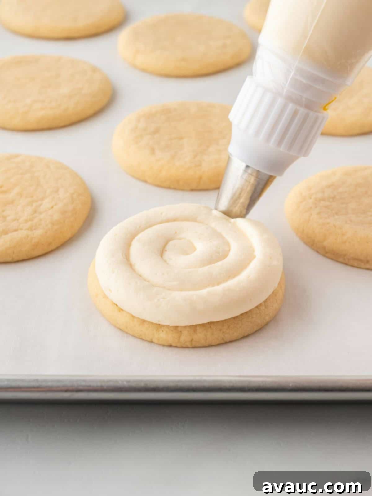 Piping white frosting onto a round sugar cookie with a piping bag and tip