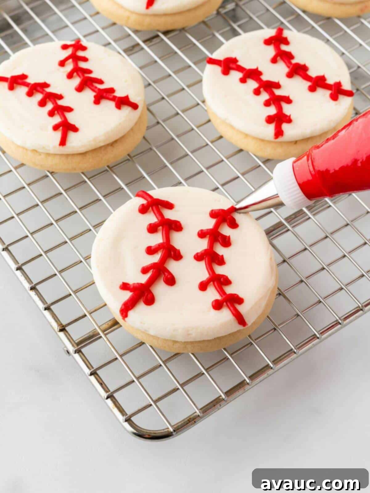 Piping red icing to create the seam and stitch details on a baseball sugar cookie