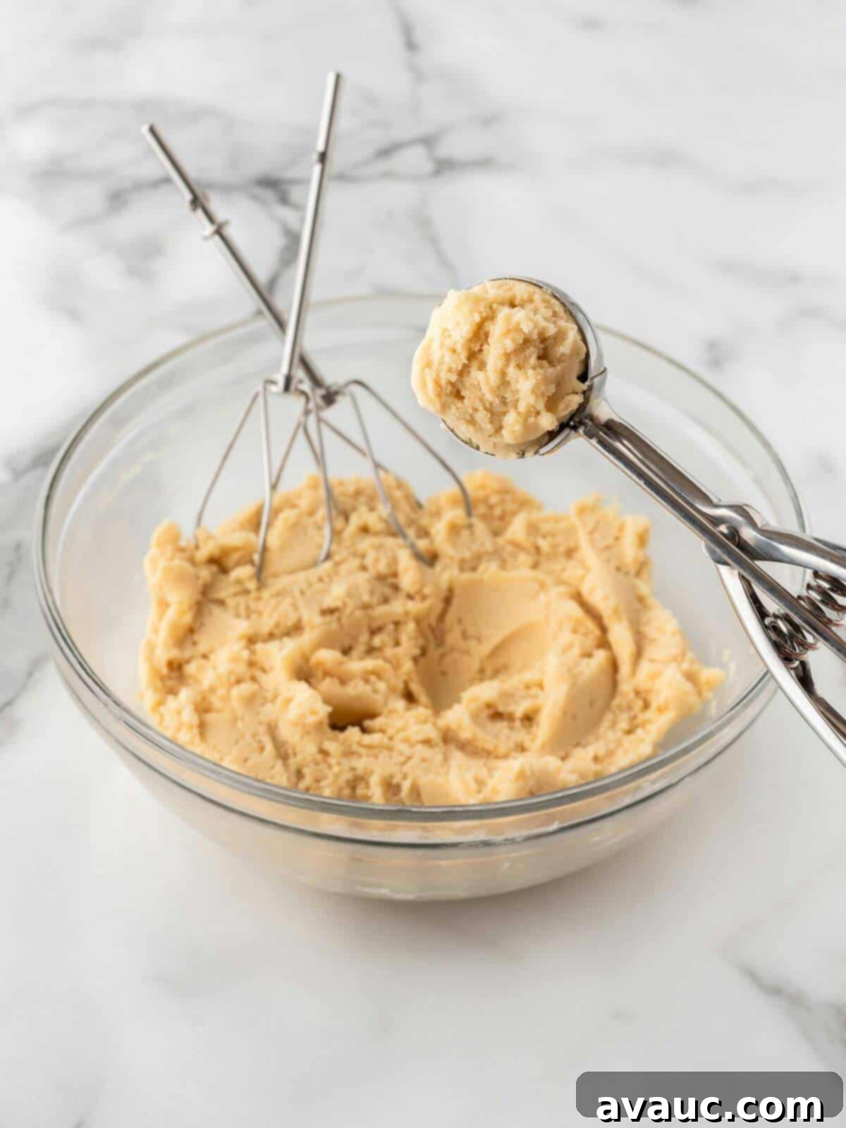 Scoops of raw sugar cookie dough in a glass bowl with a cookie scoop
